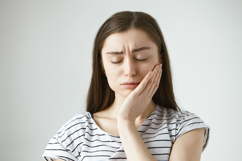 woman with a toothache; hand on cheek