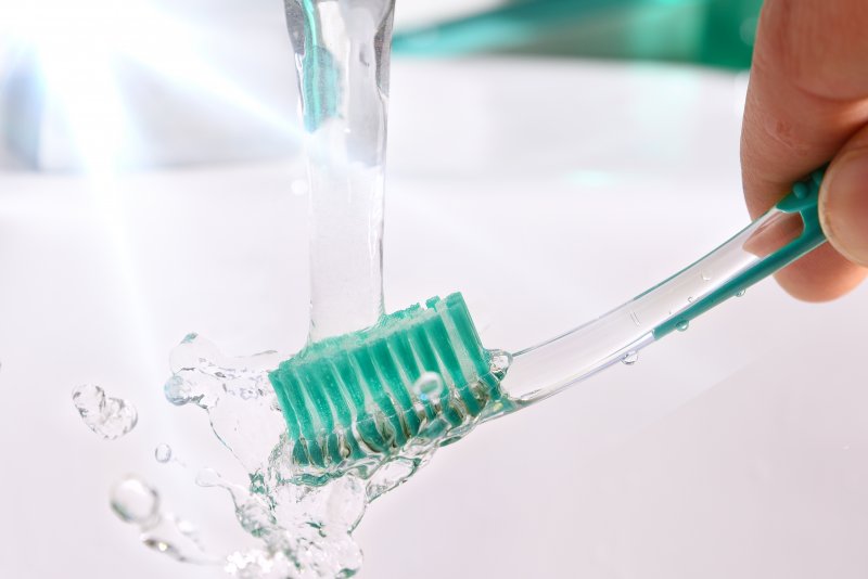 a person running their toothbrush under clean tap water to remove toothpaste and bacteria 