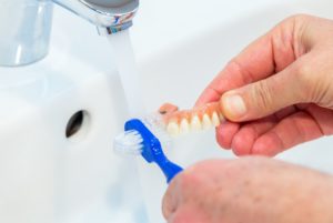 Person cleaning dentures with toothbrush