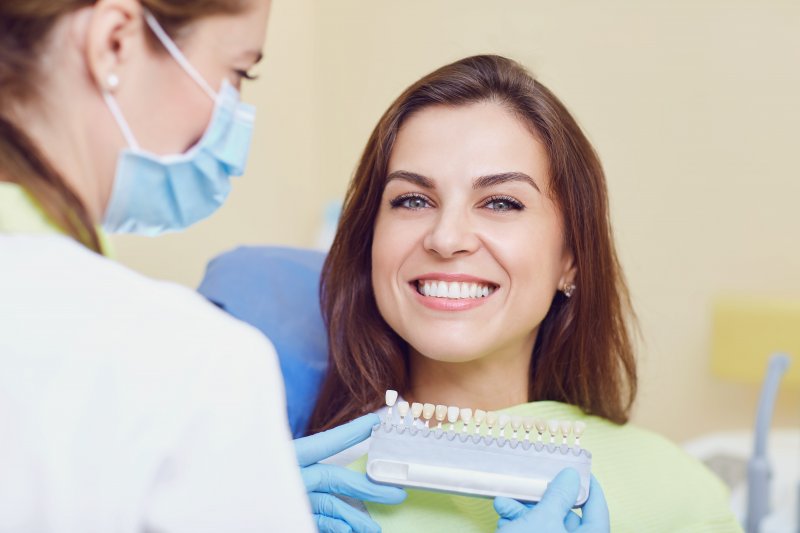 Dentist holding up veneer samples to smiling woman in dental chair