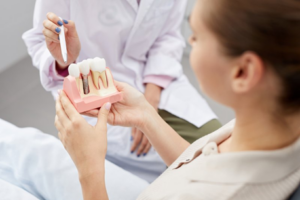 Dentist pointing to a dental implant model with a pen while patient holds the model 
